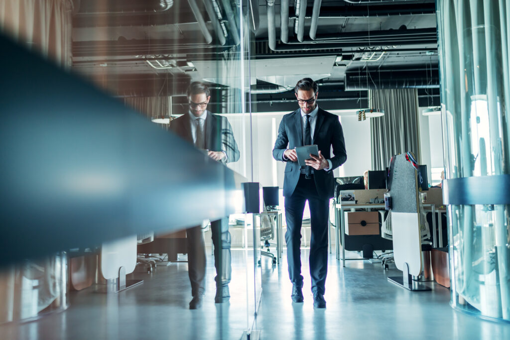Businessman walking through company and using tablet. Full length.